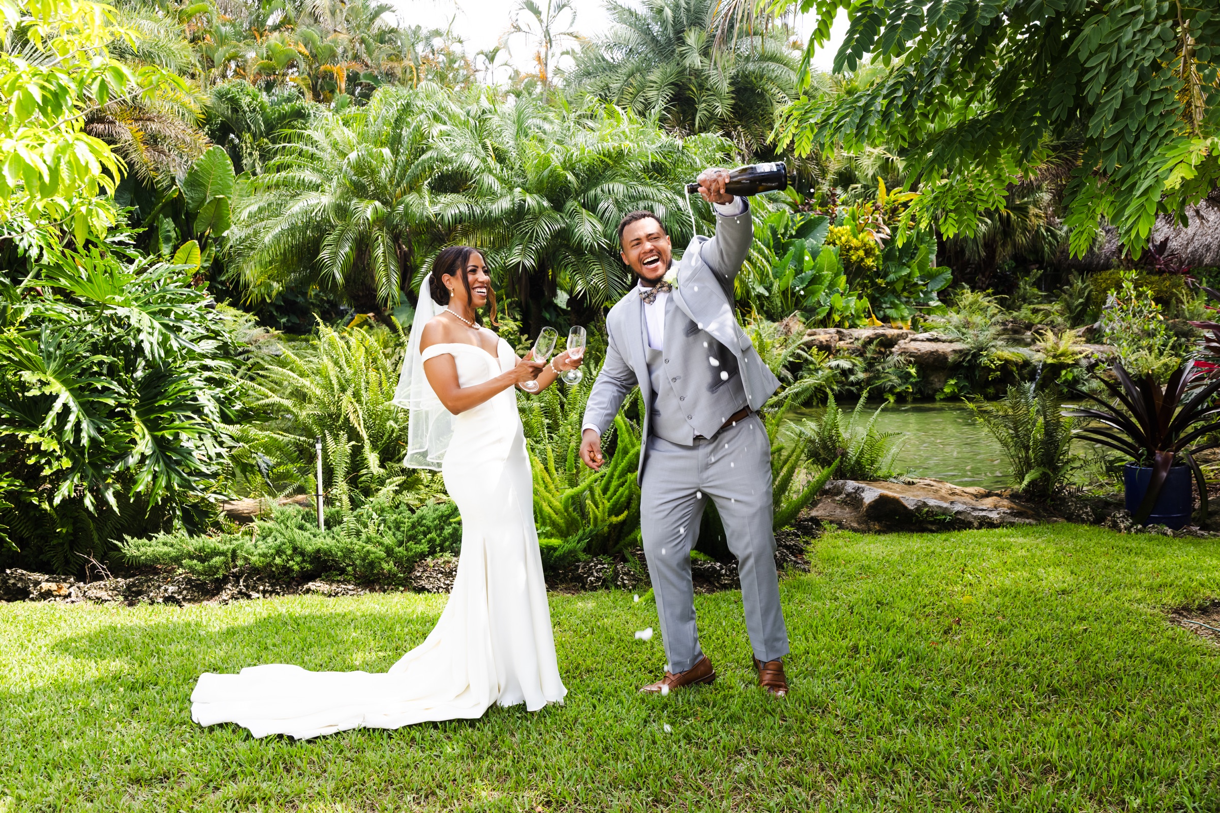 Newlyweds laughing while celebrating with champagne in a tropical garden