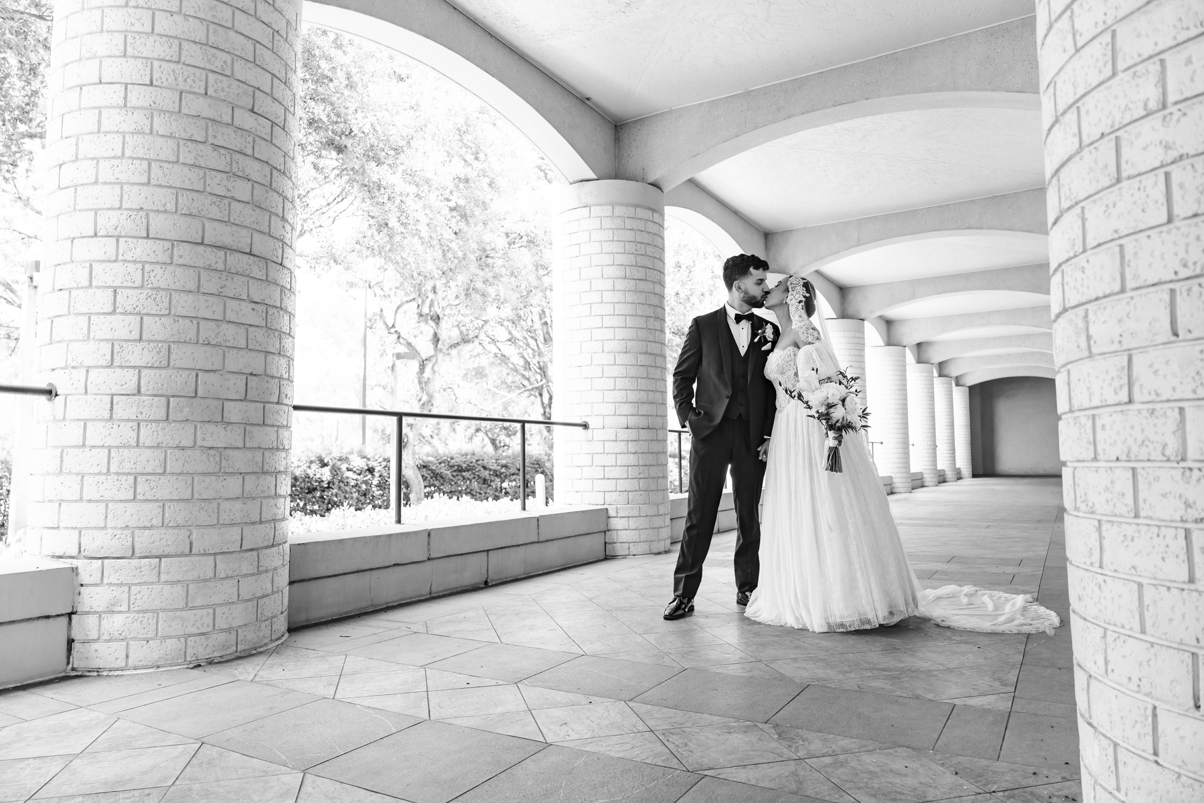 Newlyweds sharing a kiss beneath repeating architectural arches