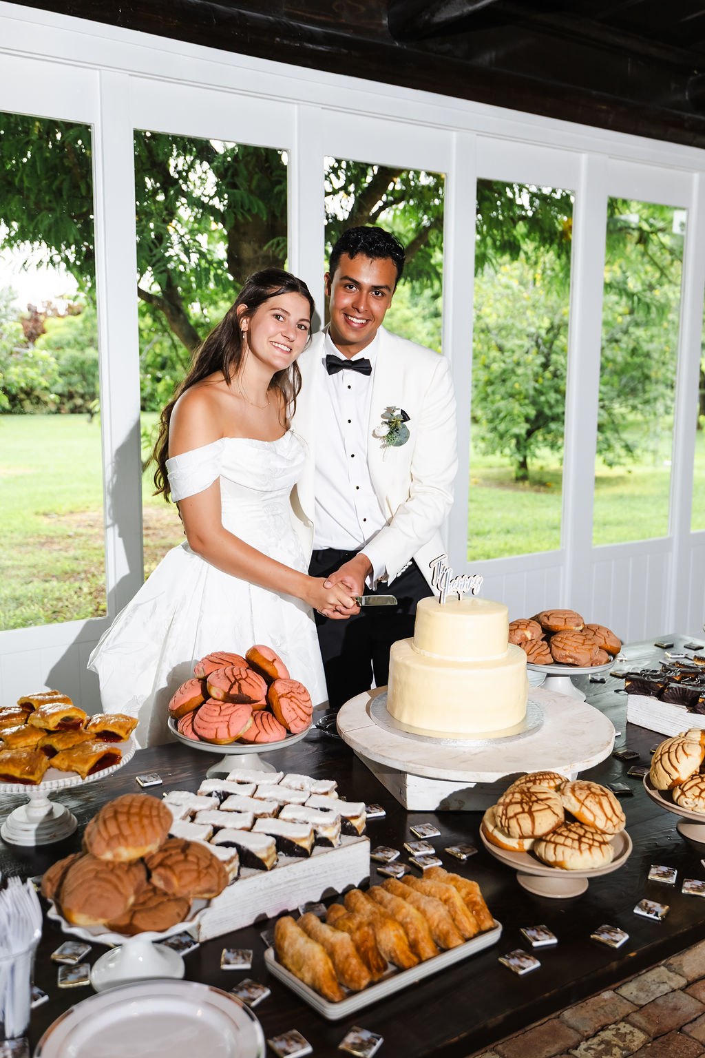 Leah and Jose beside their cake and pastry table with the garden behind them