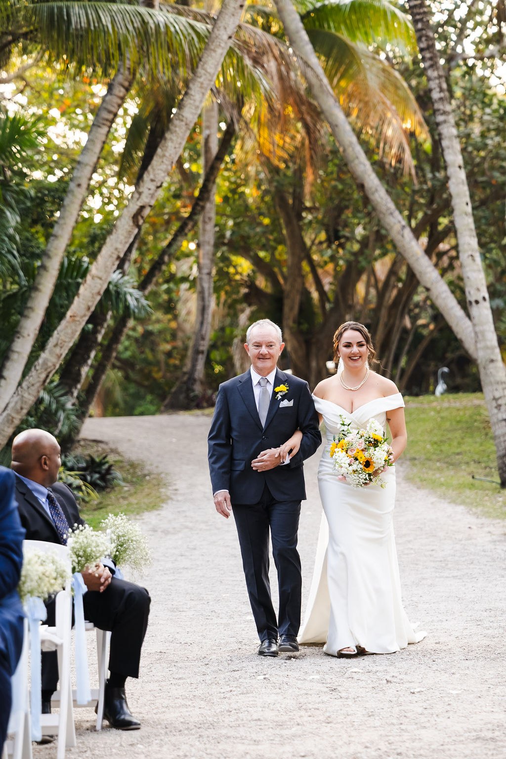 Sara walking down the palm-lined ceremony aisle with her escort