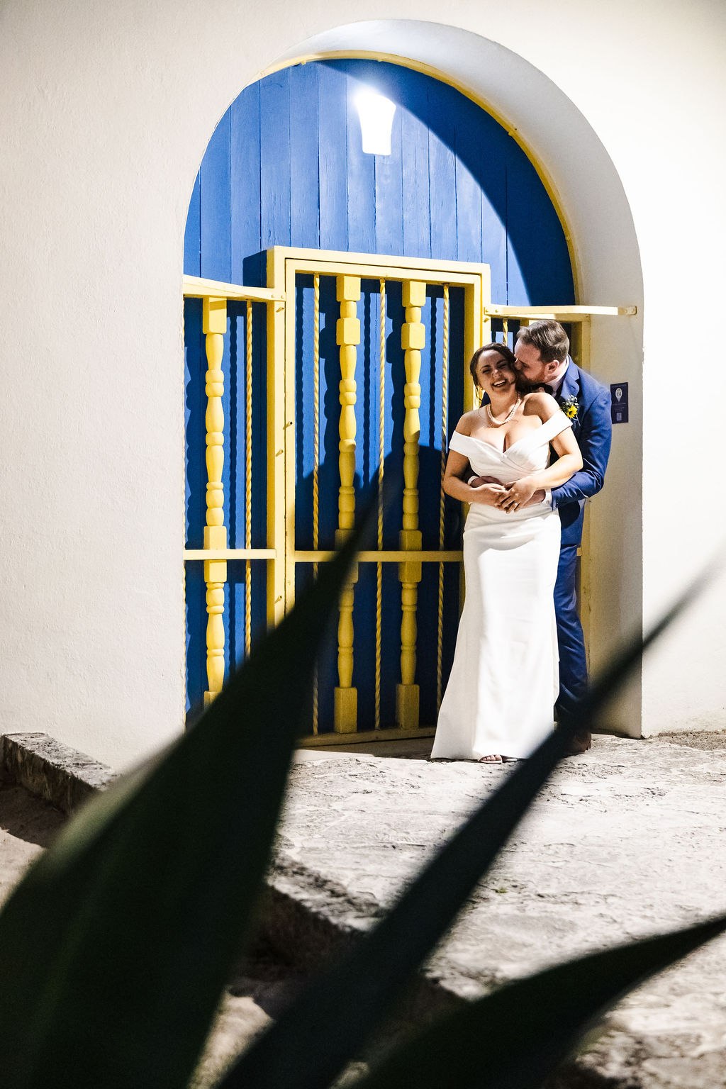 The newlyweds embracing beside a blue door and yellow railing