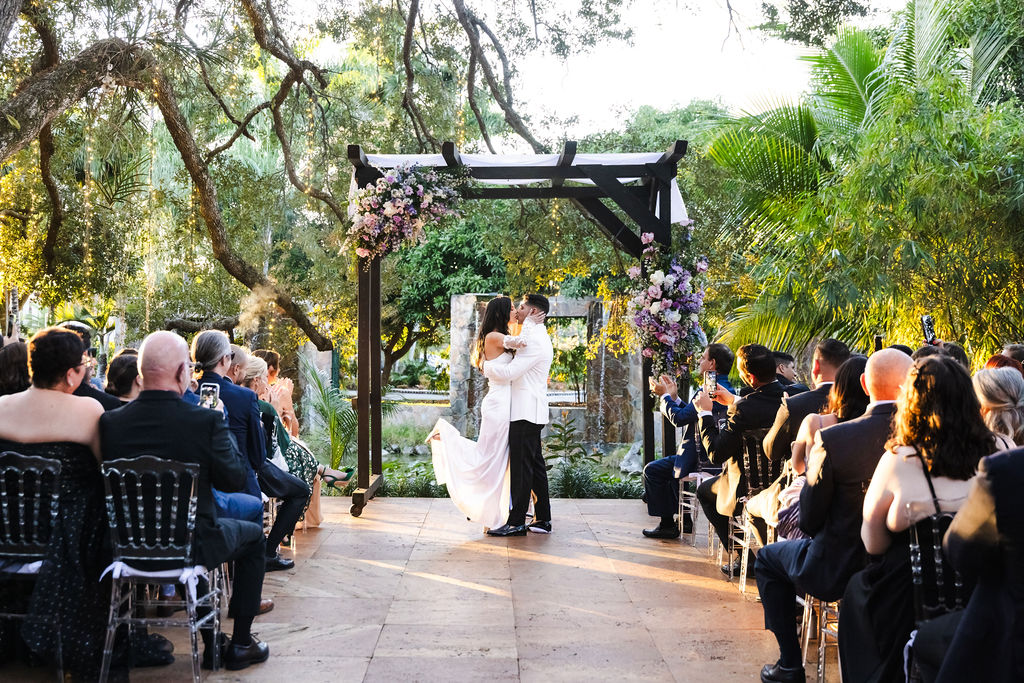 Bryn and Edward kissing beneath their floral ceremony arbor