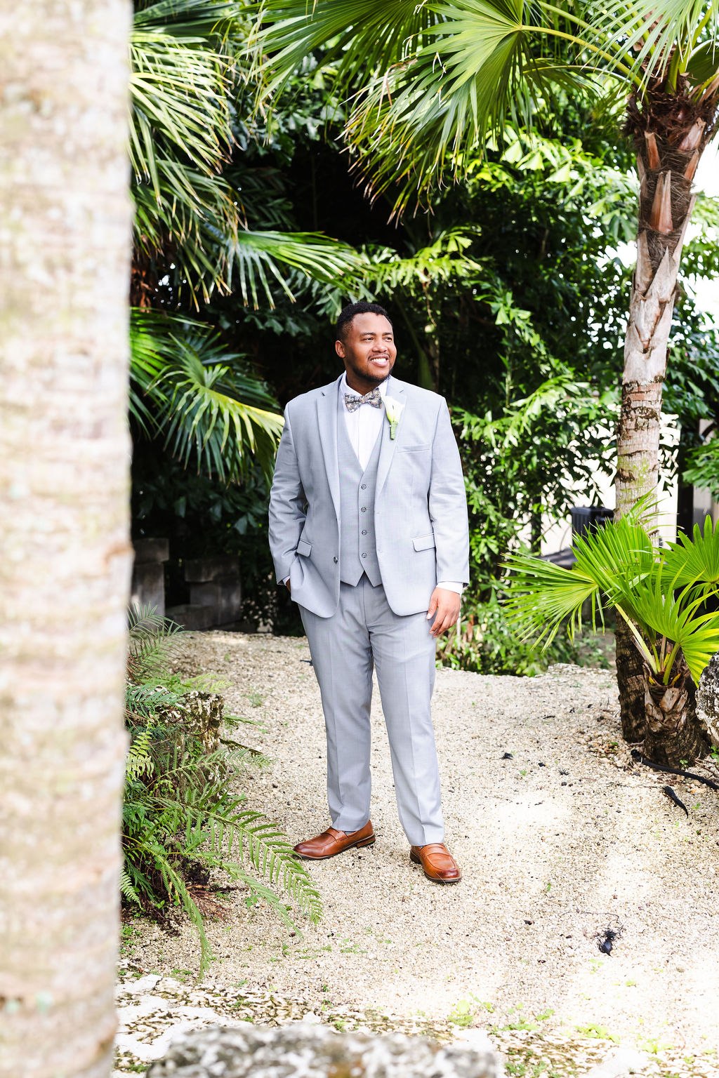 Adrian in a light gray suit beneath tropical greenery