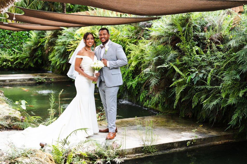 The newlyweds beside the water under a shaded garden canopy