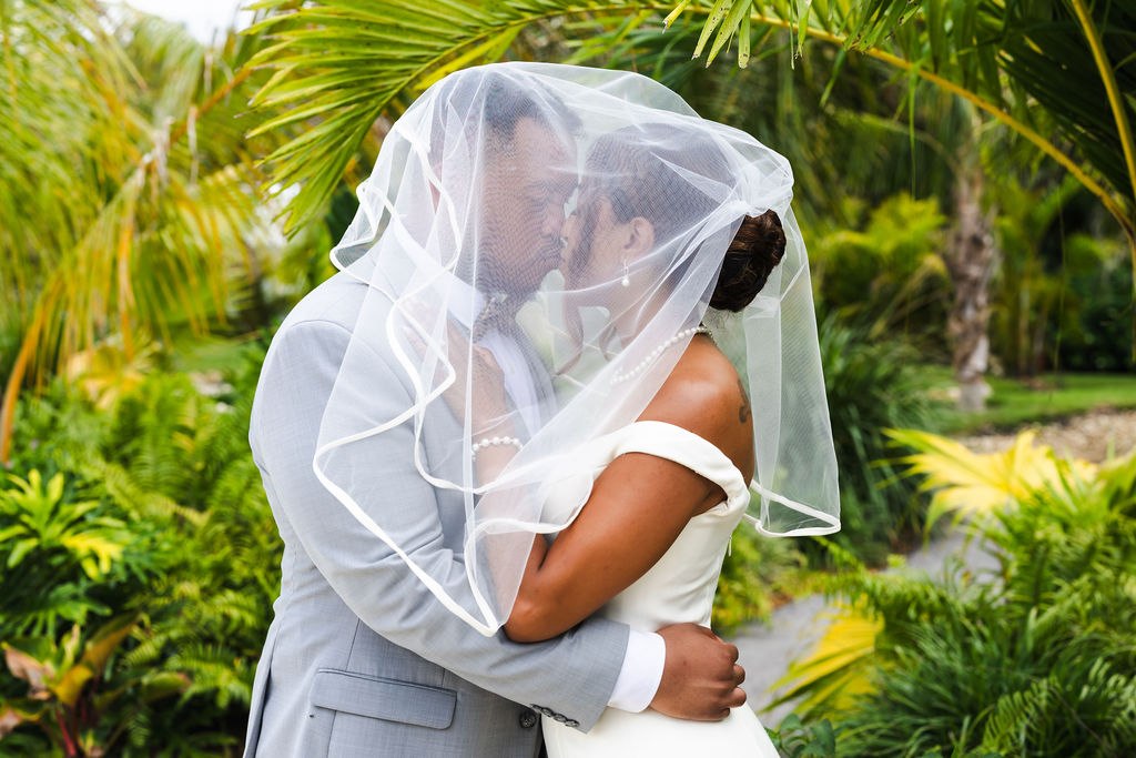 Adrian and Sharlena kissing beneath the veil among the palms