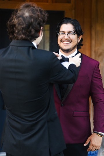 Ayrton smiling while a member of the wedding party adjusts his bow tie