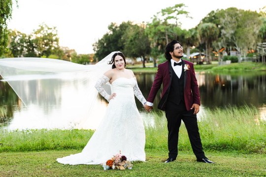 Nina and Ayrton holding hands by the pond with her veil flowing behind her