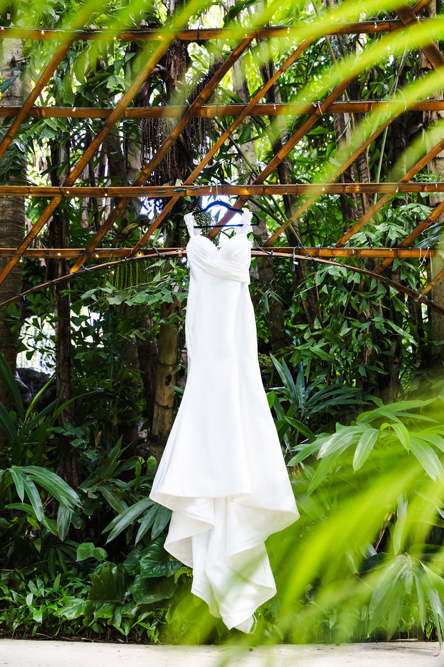 Wedding dress hanging beneath a tropical garden arbor