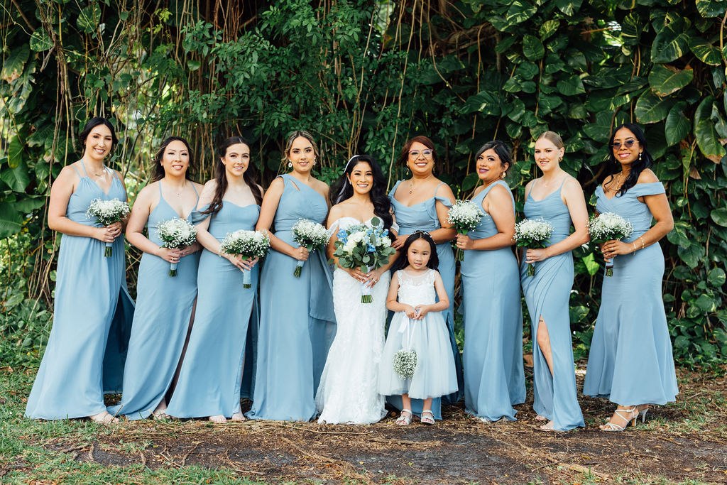 Karina and her bridal party in pale blue dresses against a leafy garden backdrop